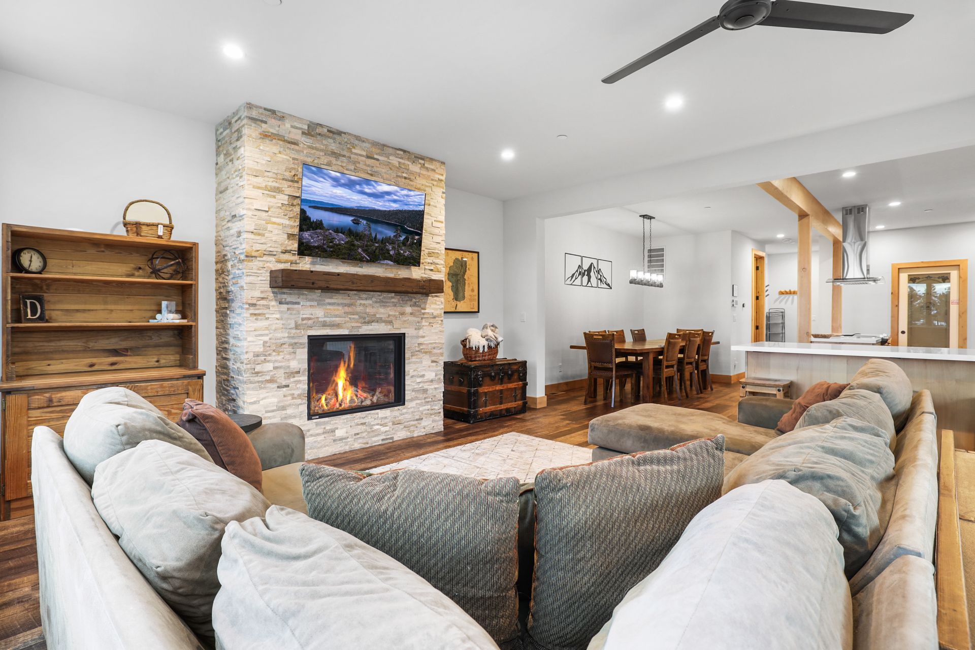 Bright living room with stone fireplace, wall TV, sectional sofa, and dining area beyond