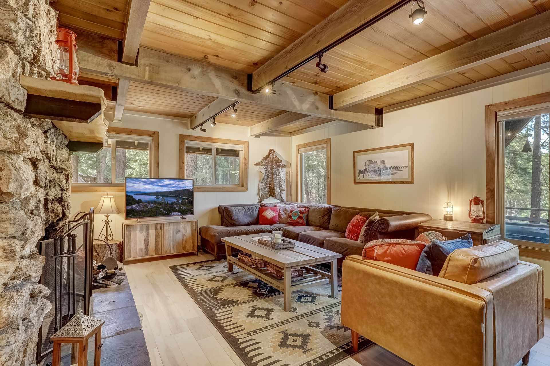 Cozy rustic living room with stone fireplace, wooden beams, and sectional sofa near a TV
