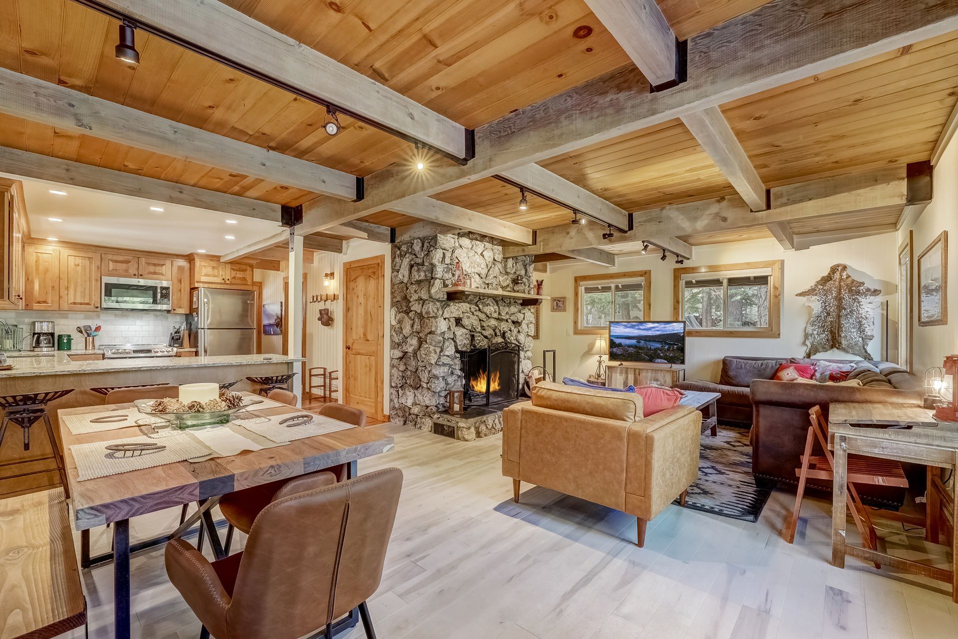 Rustic open-plan living room with stone fireplace, wood beams, and kitchen area