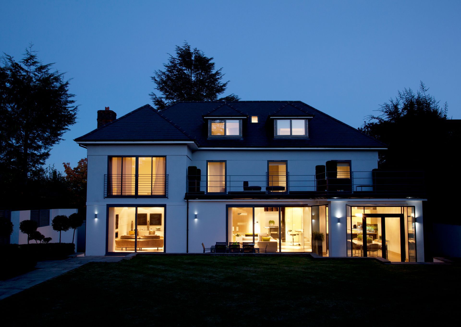 Modern two-story house at dusk with warm lights glowing from large windows