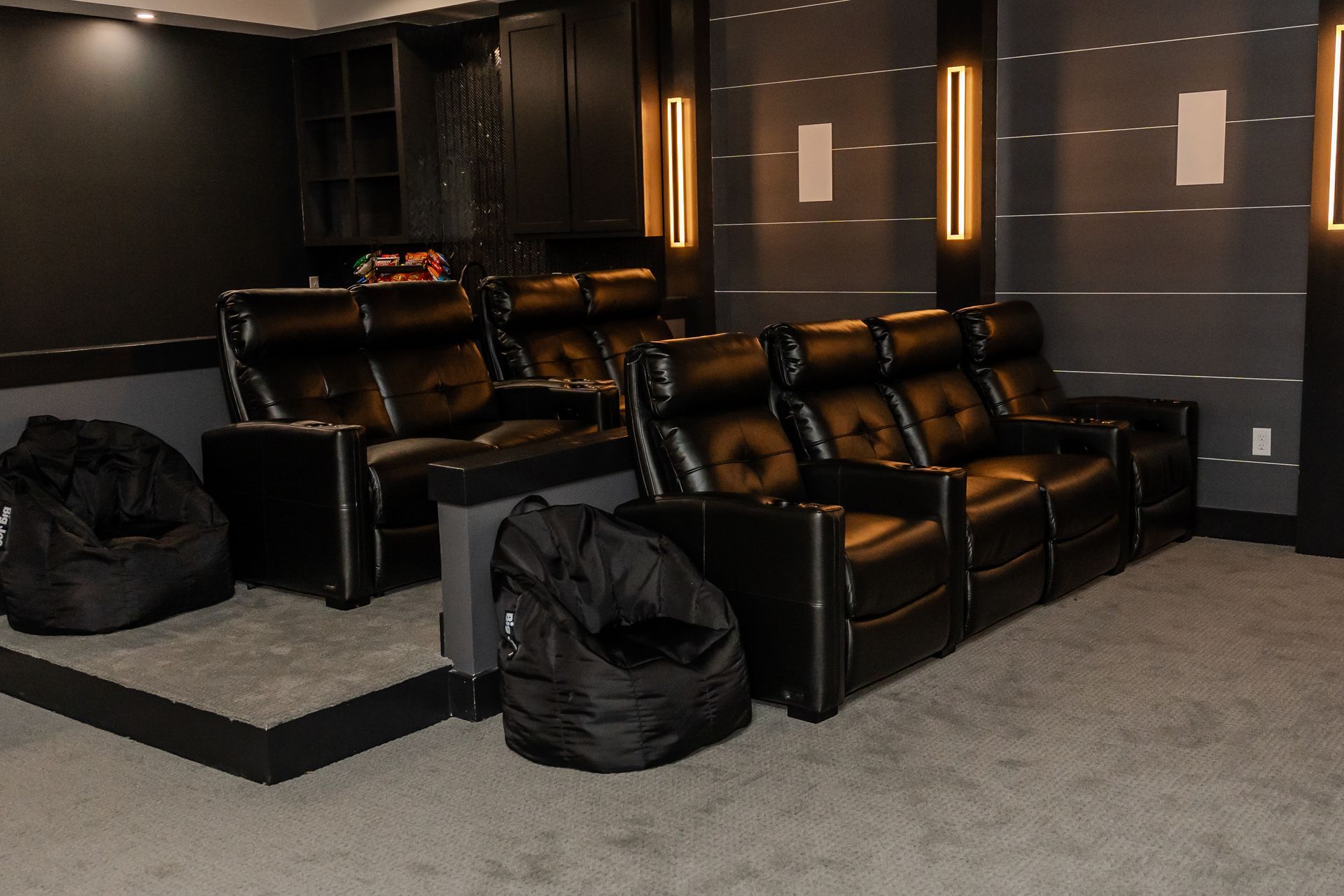 Home theater with black recliner seating, bean bags, and wall sconces in a dark room