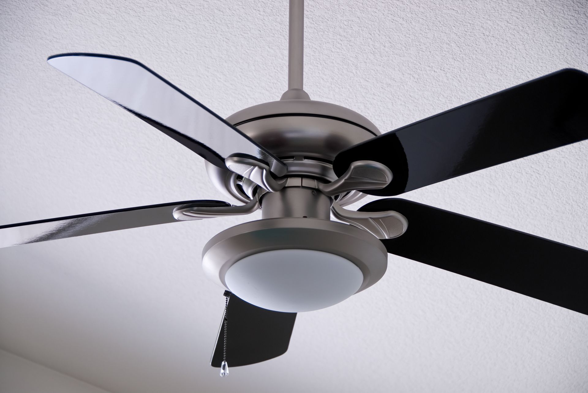Ceiling fan with four blades and a frosted light fixture on a white ceiling.
