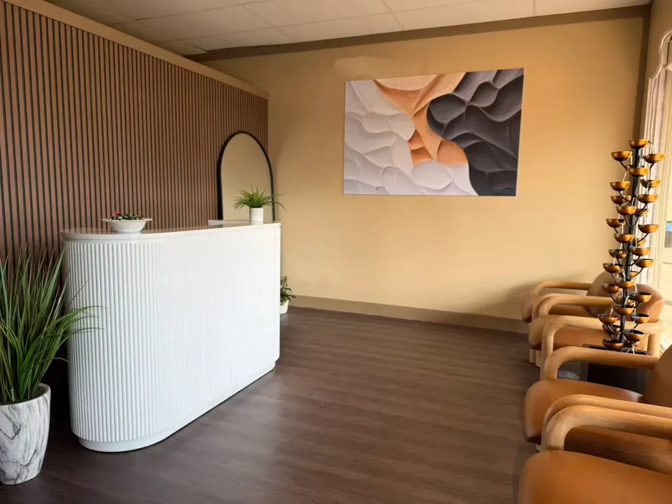 Modern waiting area with white reception desk, tan chairs, wood flooring, and abstract wall art