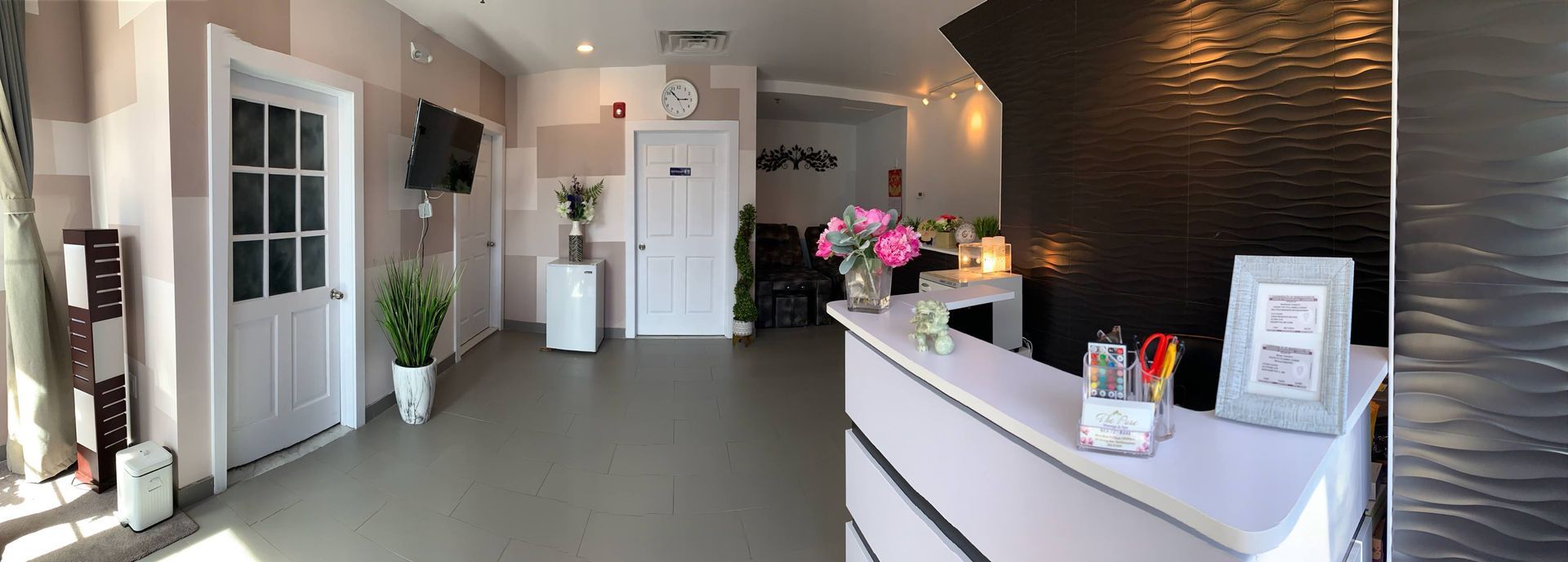 Bright salon reception with white counter, pink flowers, and black textured accent wall