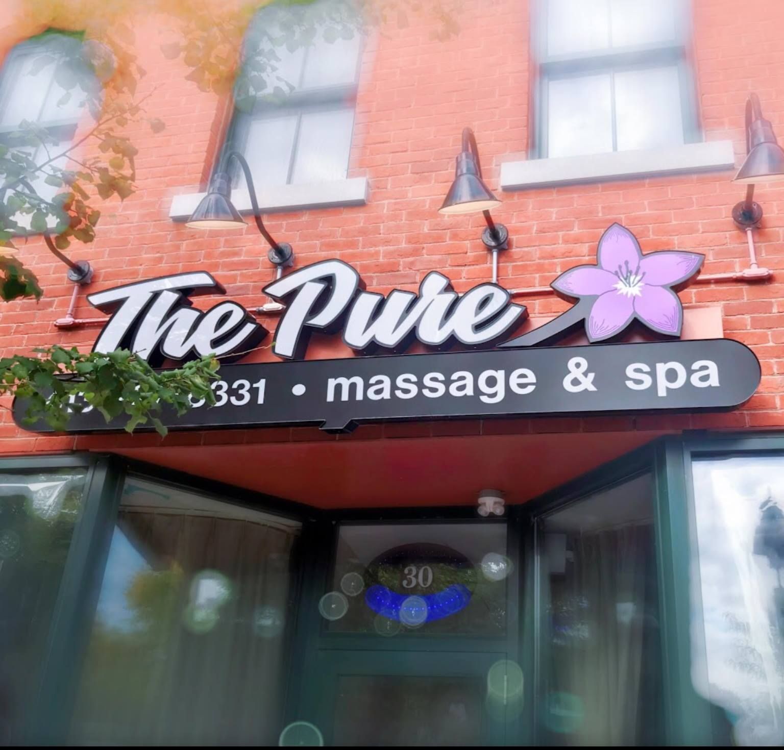 The Pure massage & spa storefront with purple flower logo on a brick building