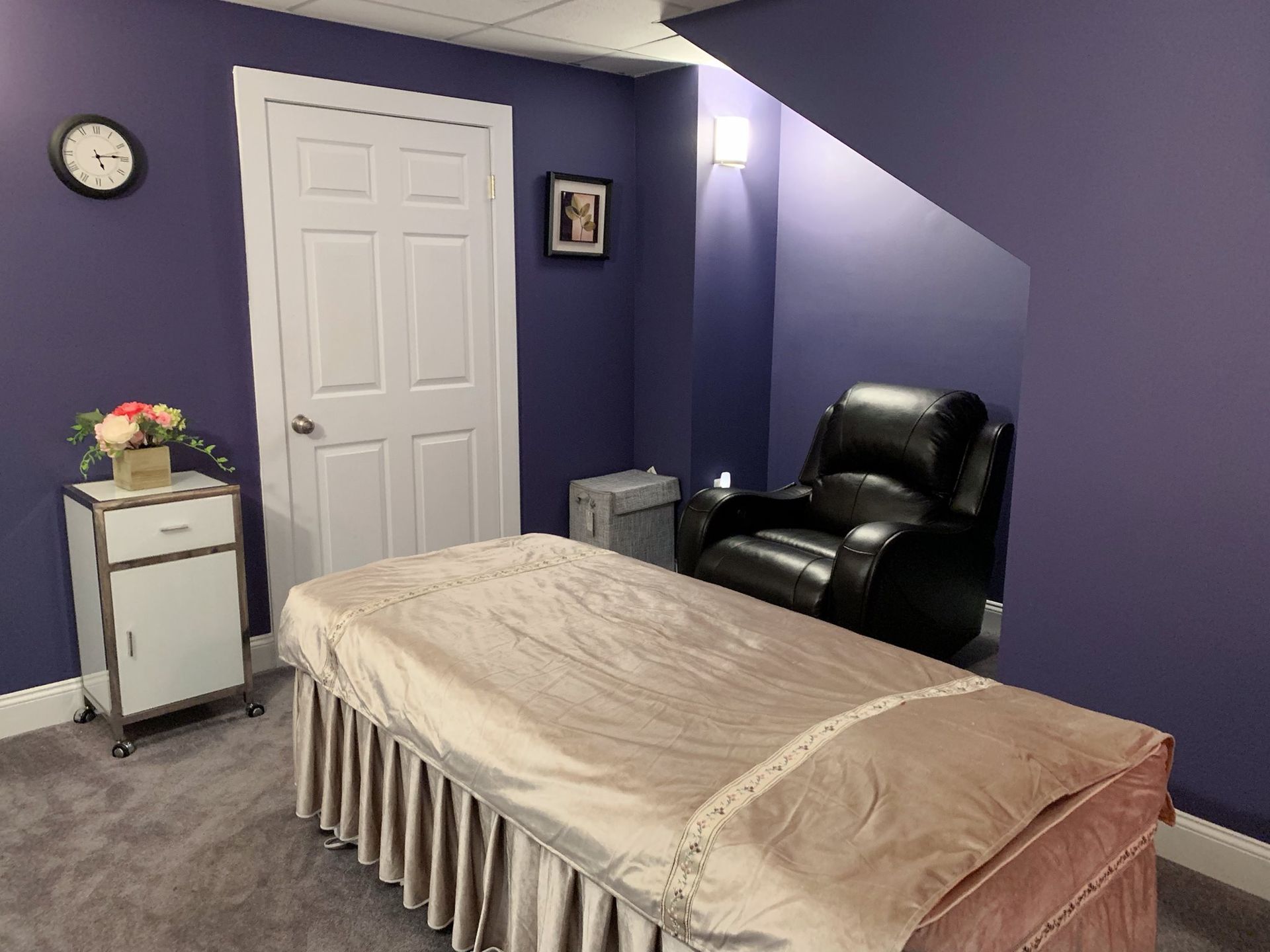 Purple bedroom with bed, black chair, white closet door, small table, and wall clock