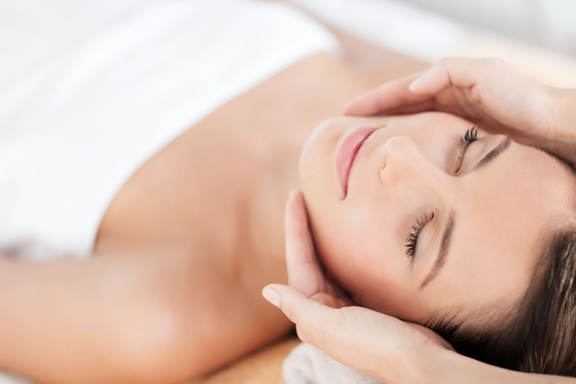 Relaxed woman receiving a facial massage with eyes closed on a white spa bed