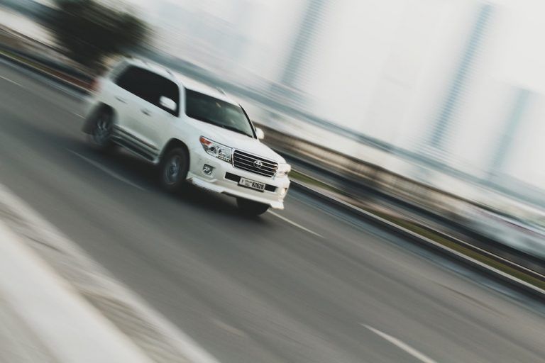 White SUV driving fast across a bridge, blurred by motion