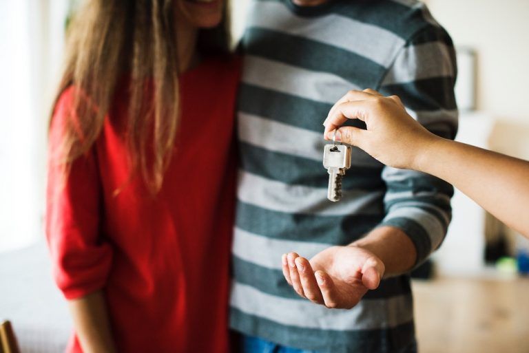 Person holding out a key in front of a couple standing together indoors