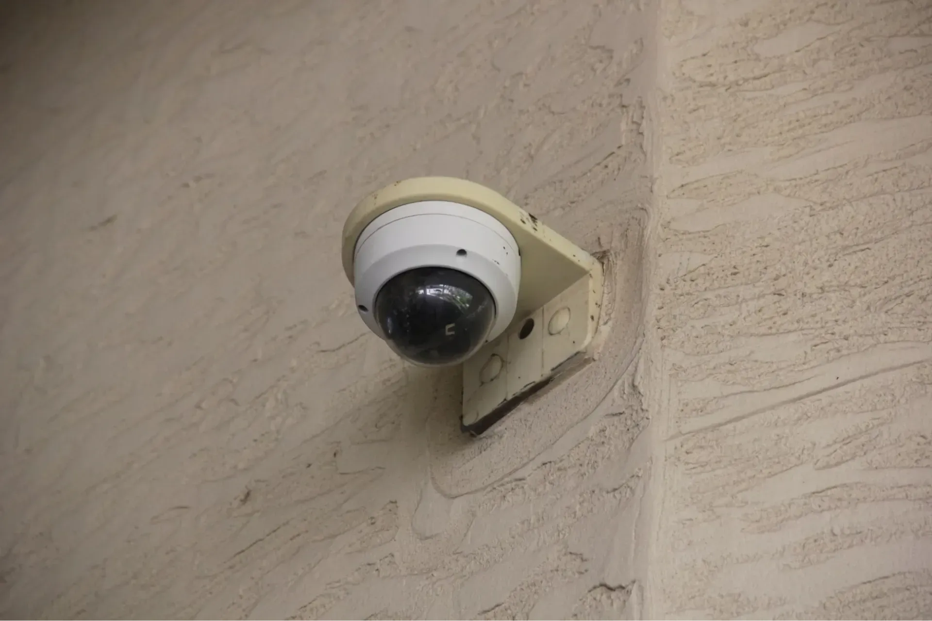 A circular security camera mounted on a stucco wall. 