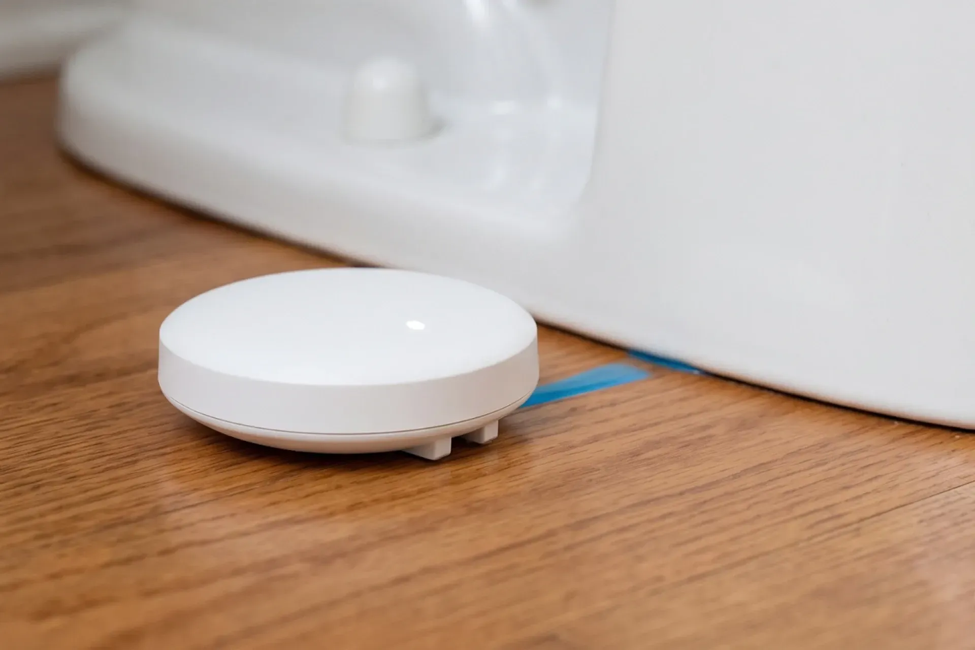 A modern water leak sensor device placed on a bathroom floor near a toilet base.