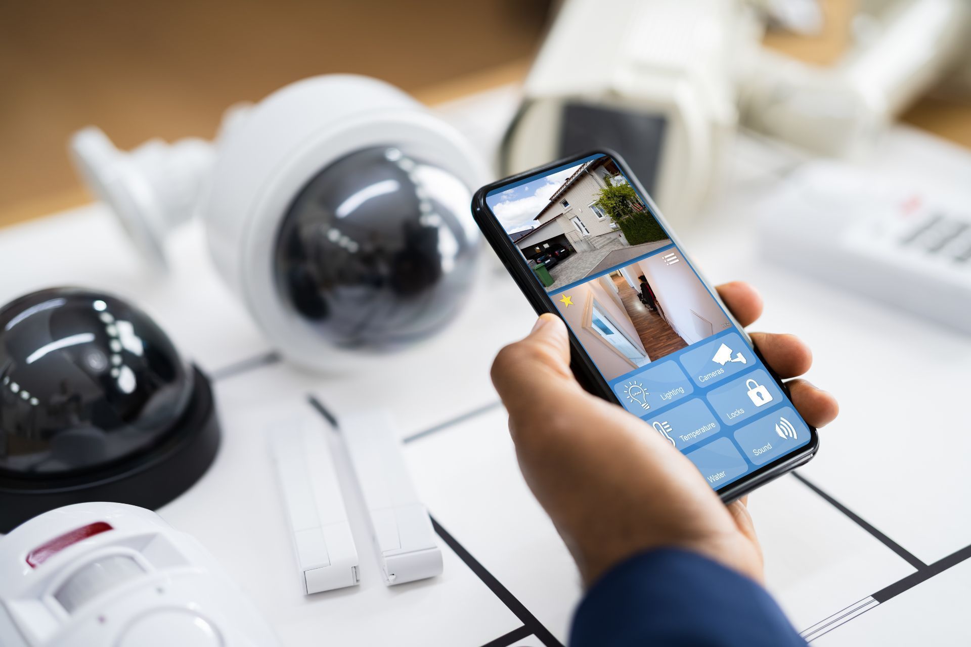 Person holding a smartphone showing security feeds of the interior and exterior of their home