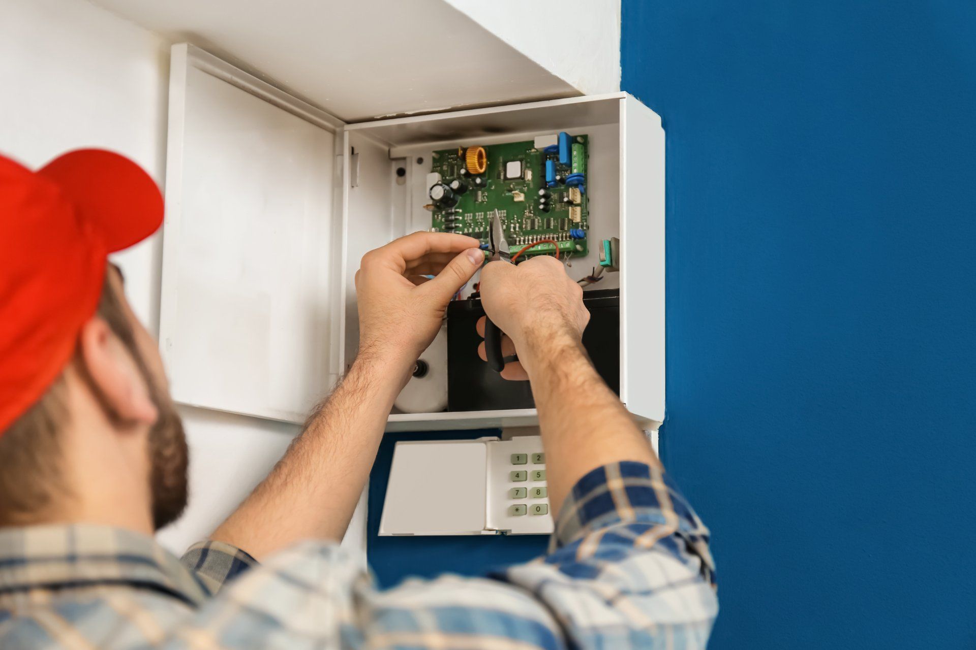 Technician providing professional installation services, adjusting wiring inside a home security alarm panel.