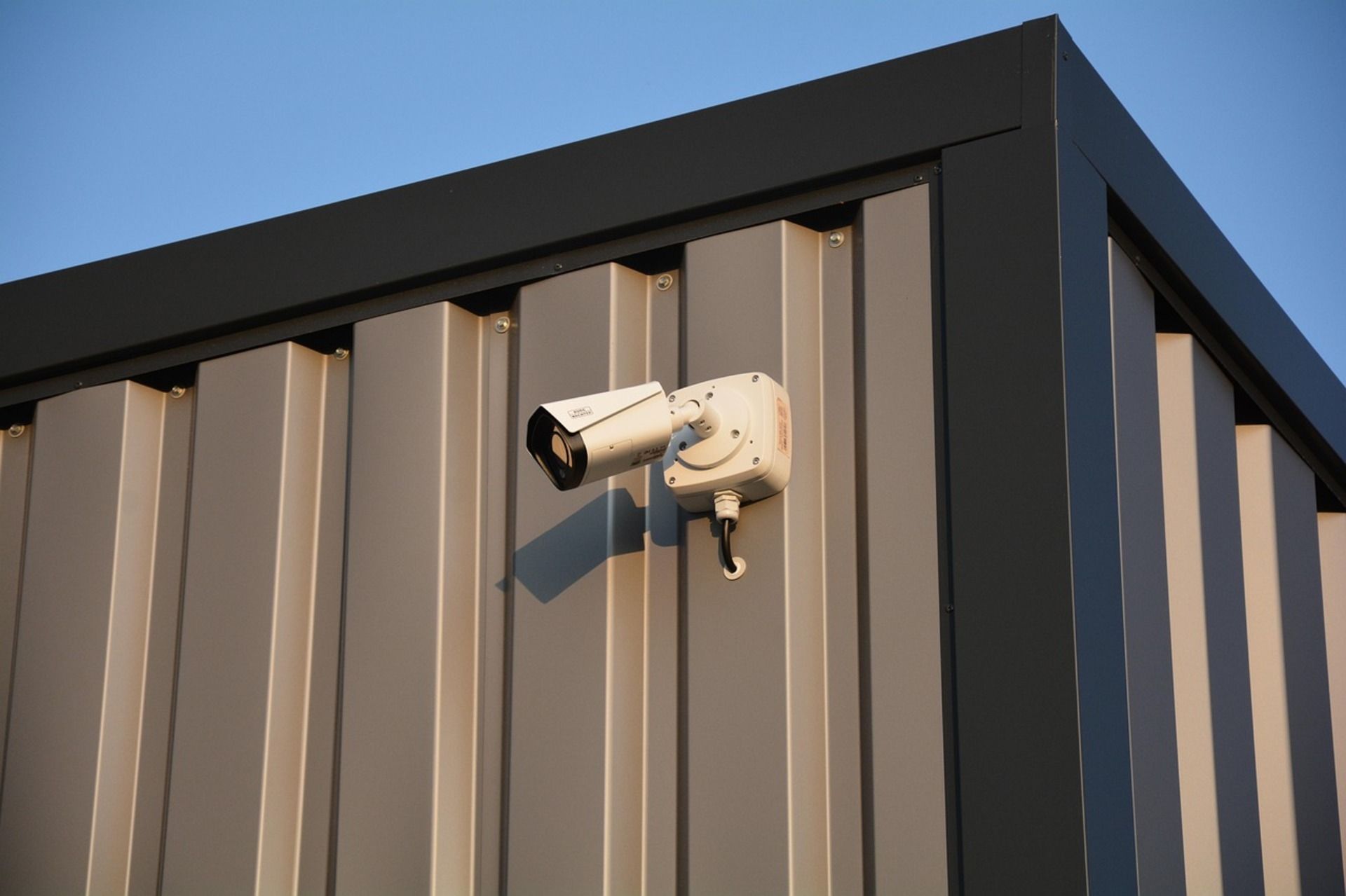 An outdoor security camera mounted on a warehouse wall is pointed to the side.