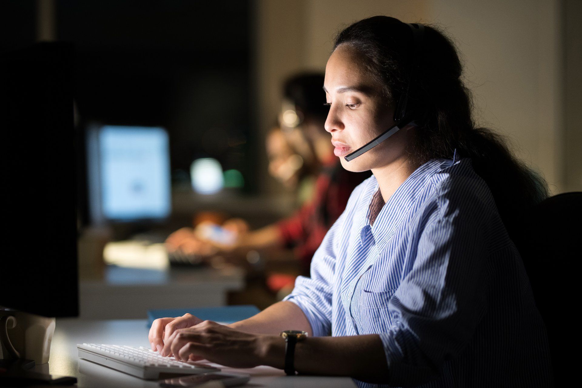 A monitoring service representative wearing a headset and working on a computer in a dimly lit office