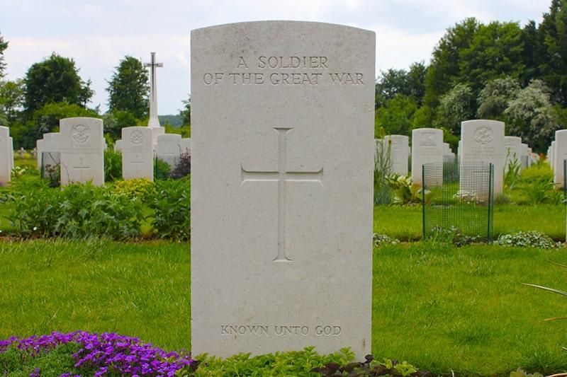 Military cemetery headstones in green grass, with a central white stone marked by a cross.