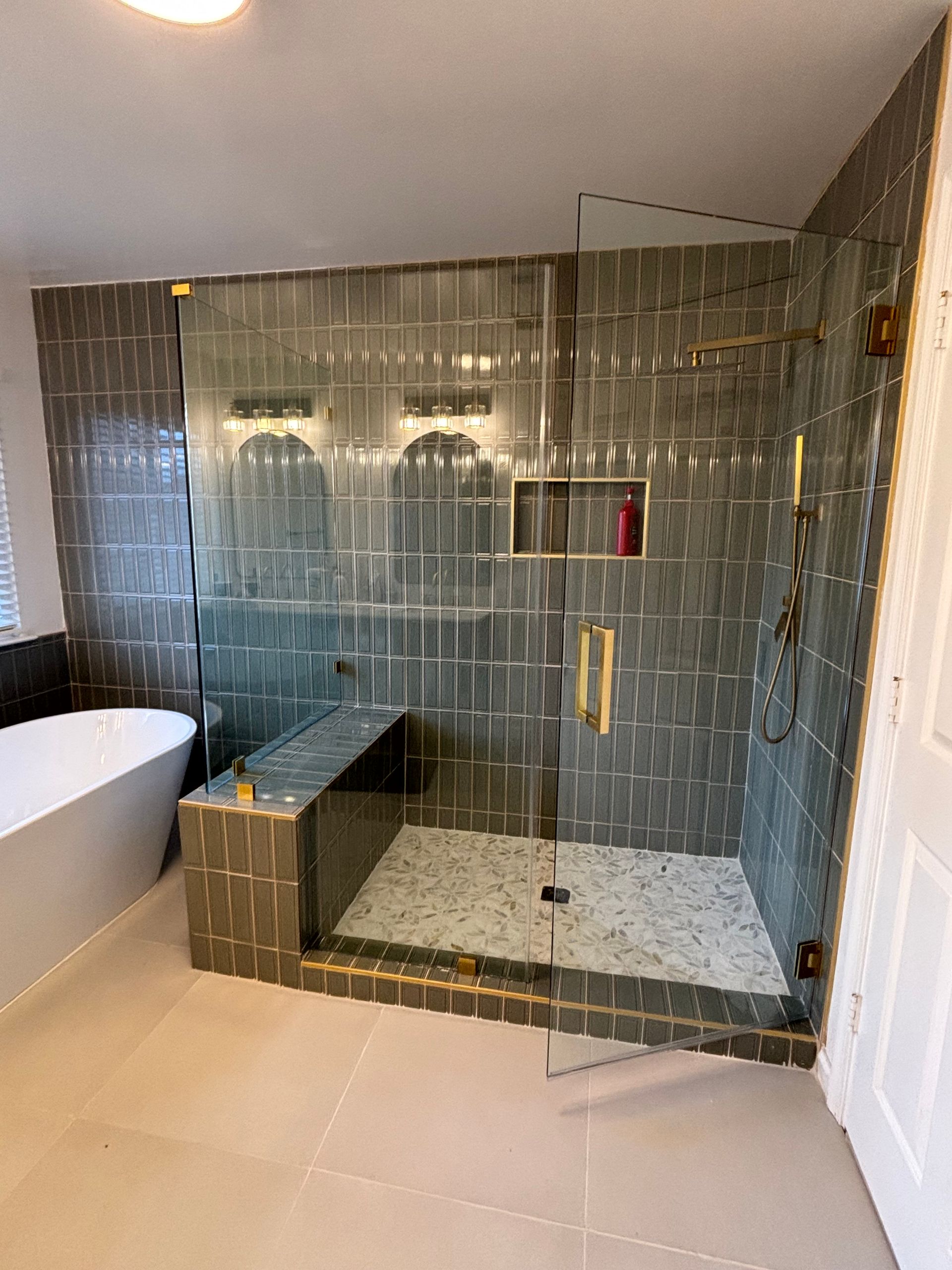 Modern bathroom with a large walk-in shower. Gray tiled walls, glass doors, and a bench.