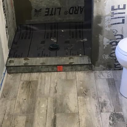 An unfinished bathroom shower stall with a grey tiled curb and dark waterproof underlayment, viewed from the floor.