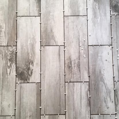 Light gray, wood-grain ceramic floor tiles partially installed with white plastic spacers between them.