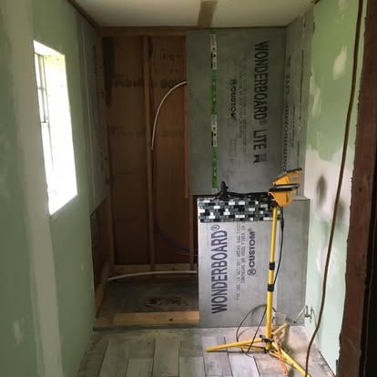 A bathroom undergoing renovation featuring Wonderboard cement backer board installed on shower walls, with a work light.