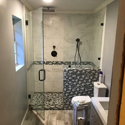 A modern bathroom with a glass-enclosed shower, featuring white marble tiles and a black-and-white mosaic accent wall.