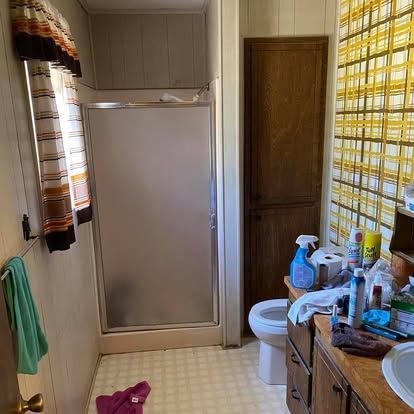 A bathroom with a shower, a wood cabinet, a toilet, a vanity, and yellow-patterned wallpaper.