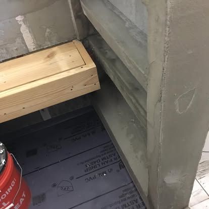 A wooden bench frame sits inside a shower alcove during construction, next to grey waterproof wall panels and floor liner.