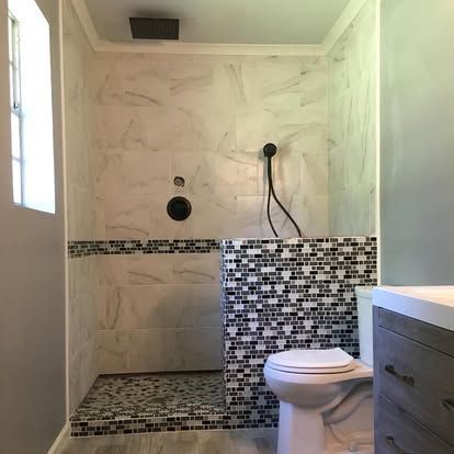A walk-in shower with marble-look walls and a mosaic tile base, positioned next to a toilet in a modern bathroom.