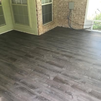 Gray wood-look flooring installed in a sunroom with brick walls and large windows.