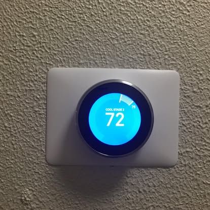 A Google Nest smart thermostat with a bright blue circular display showing a temperature of 72 degrees against a wall.