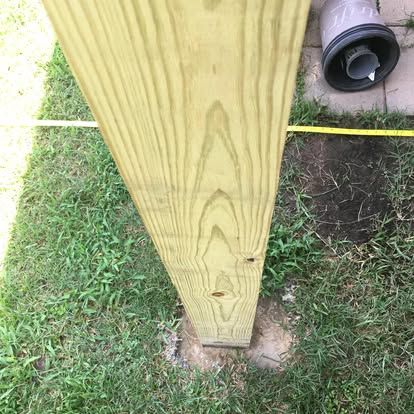 A wooden post set in a concrete base in a grassy area, with a yellow tape measure extending across the ground nearby.