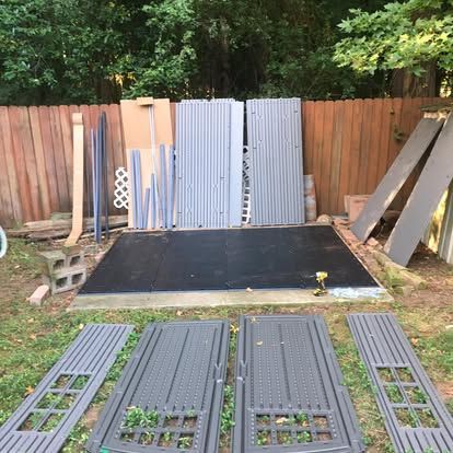 Pre-fabricated shed panels and components arranged on a concrete foundation in a backyard.