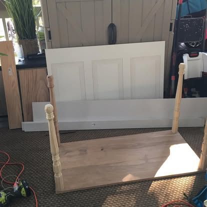 An unfinished wooden table top with four turned legs is upside down on a patio, with furniture parts resting behind it.