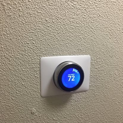 A Nest smart thermostat on a textured beige wall, showing a blue display set to 72 degrees.