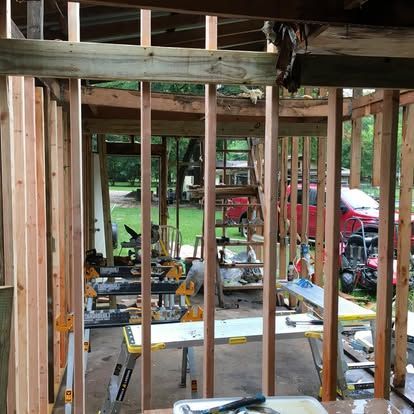 An interior view of a room under construction, showing wooden wall studs, a wooden header beam, and work benches.