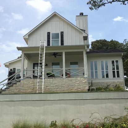 A two-story white farmhouse with a stone foundation, front porch, and ladder leaning against the second story.