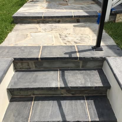 Stone steps with dark rectangular treads and light-colored irregular flagstone landings, flanked by white stucco walls.