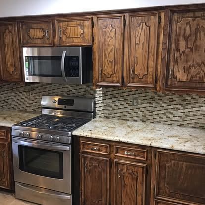 A kitchen scene featuring dark wood cabinets, a stainless steel microwave and oven, and a patterned, earth-toned backsplash.