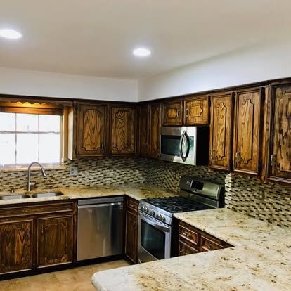 A modern kitchen with dark wood cabinets, granite countertops, stainless steel appliances, and a mosaic backsplash.