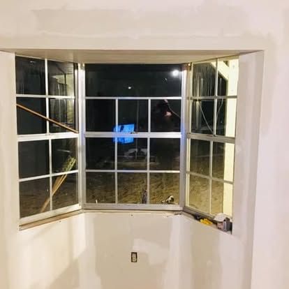 A three-paneled bay window with white trim, installed in an unfinished room with drywall and an electrical outlet.
