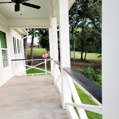 A white porch with a ceiling fan, X-style railings, and a view of a green lawn and trees.