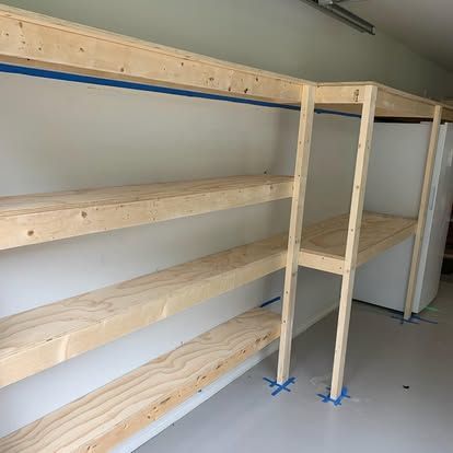 Unfinished wooden shelving unit installed in a garage next to a white refrigerator.