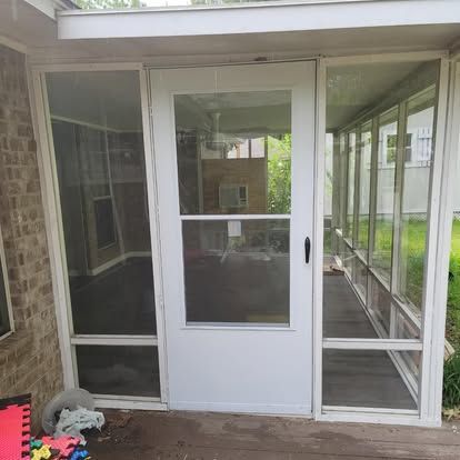 A white storm door with glass panels centered between two floor-to-ceiling glass-paneled walls on a porch.