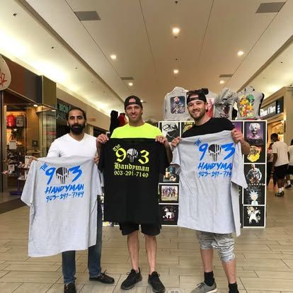 Three people in a shopping mall hold up shirts with 