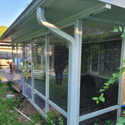 A screened-in patio or sunroom enclosure with white framing, visible against the exterior wall of a house.