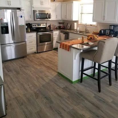 A bright, modern kitchen featuring white cabinets, stainless steel appliances, a center island, and wood-look flooring.