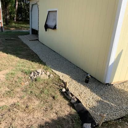 Yellow building exterior with a gravel pathway along the wall, featuring black landscape fabric and scattered rocks.