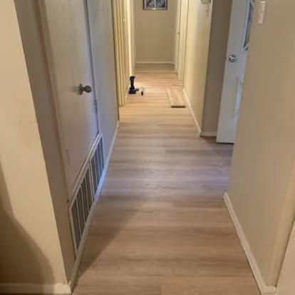 A hallway with light wood-look flooring, beige walls, white doors, and a floor-level vent.