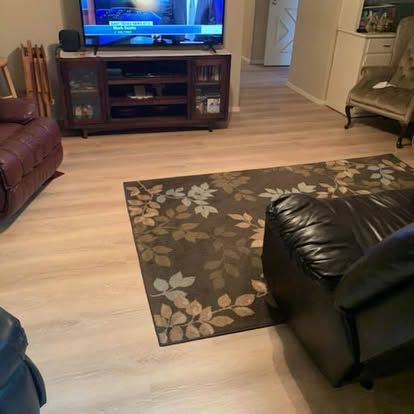 A living room with light wood floors, a patterned rug, a dark media console with a TV, and partial views of leather chairs.