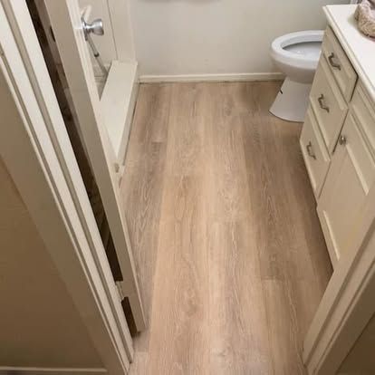 A modern bathroom with light wood-look flooring, cream-colored vanity cabinets, and a white toilet.